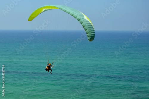 man is flying on green paraglider in the sky above the azure sea. .Balance, extreme sports, active lifestyle. Mediterranean Sea, Israel