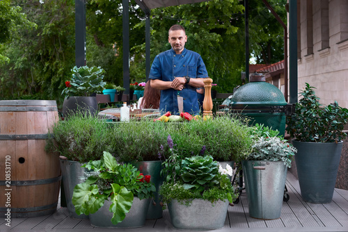 beautiful European-looking chef standing at restaurant terrace, slicing vegetables and looking at camera photo