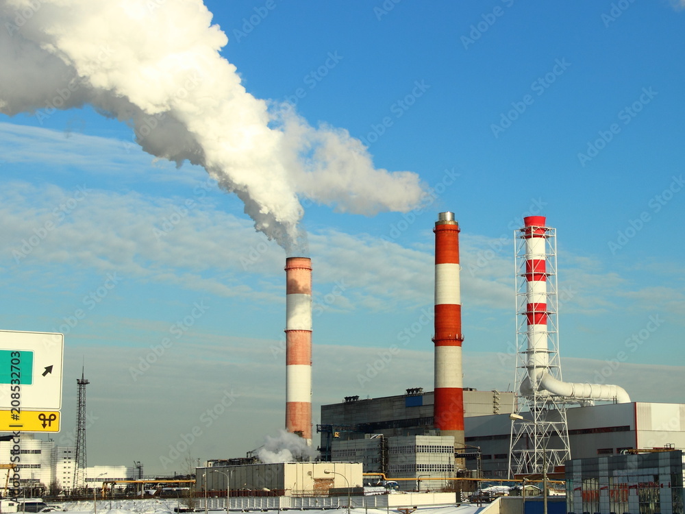 Industry, industry and ecology - grey-white smoke from the red-white pipes of the plant (chemical plant power plant), thermal power plant against the blue clear sky