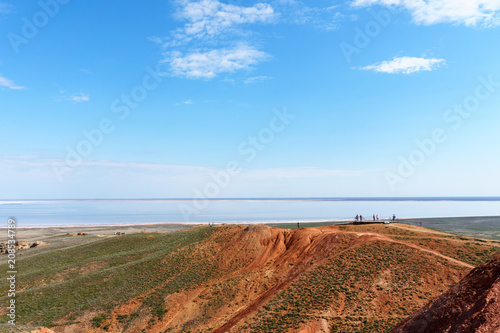 view from afar  people on the observation deck on the unusual red mountain look at the blue lake and steppe