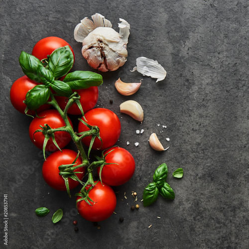Food background. Flat lay of fresh tomatoes with basil, garlic and seasalt on black stone background. Square crop, top view.