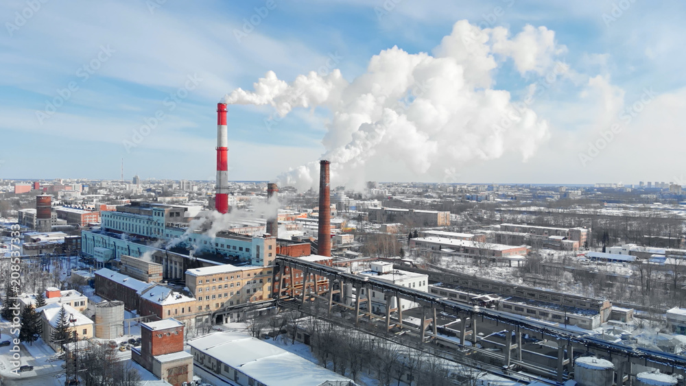 Dense thick smoke coming from industrial red-white pipes. Smooth aerial shooting of a power plant from a bird's eye view. Industrial environmental pollution with the fume. Dense thick smoke coming from industrial red-white pipes. Smooth aerial shooting of a power plant from a bird's eye view. Industrial environmental pollution with the fume.