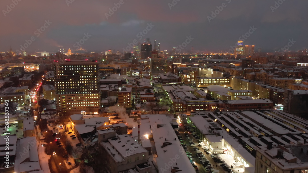 Aerial flight shot above Moscow night city lights. Cold evening winter Russian city with old soviet buildings and modern skyscaper, cityscape view.