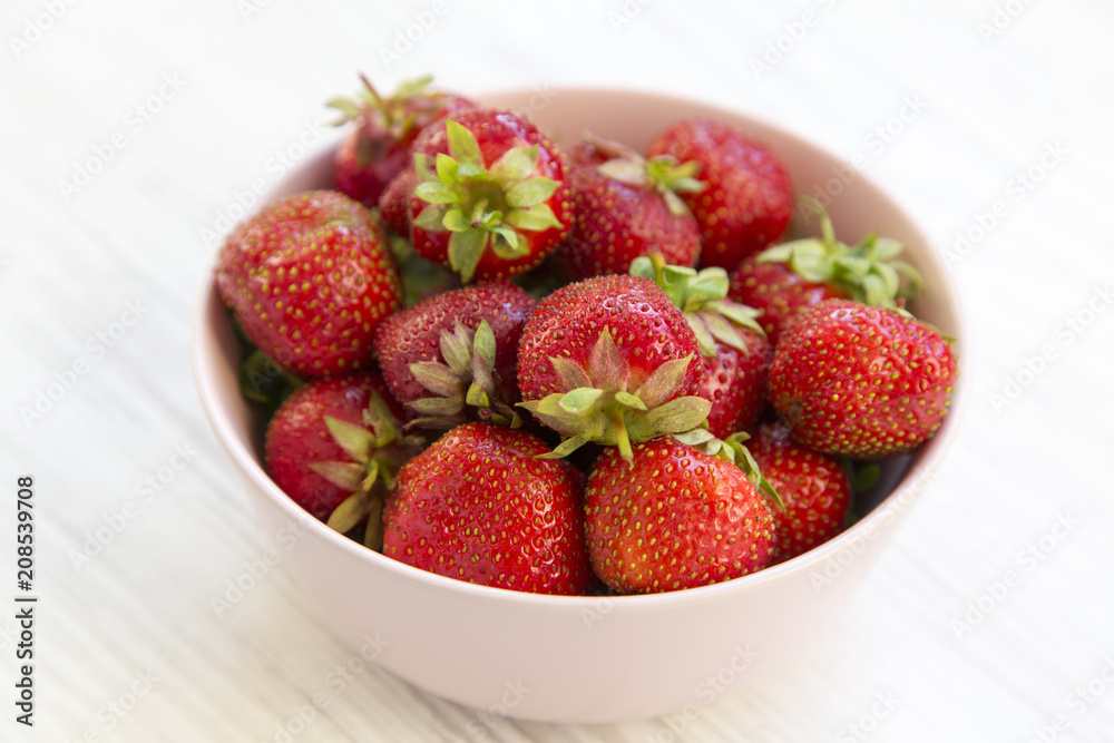 Fresh strawberries in a pink ceramic bowl on white wooden table, side view. Fresh strawberries in a pink ceramic bowl on white wooden table, side view.
