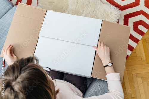 Woman unboxing cardboard box online e-commerce site delivery  - view from above in living room photo