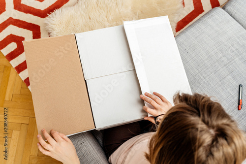 Curious woman unboxing cardboard box online e-commerce site delivery  - view from above in living room photo