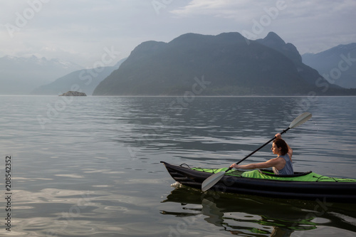 Woman kayaking around the beautiful Canadian Mountain Landscape during a vibrant cloudy evening. Taken in Howe Sound  North of Vancouver  British Columbia  Canada.