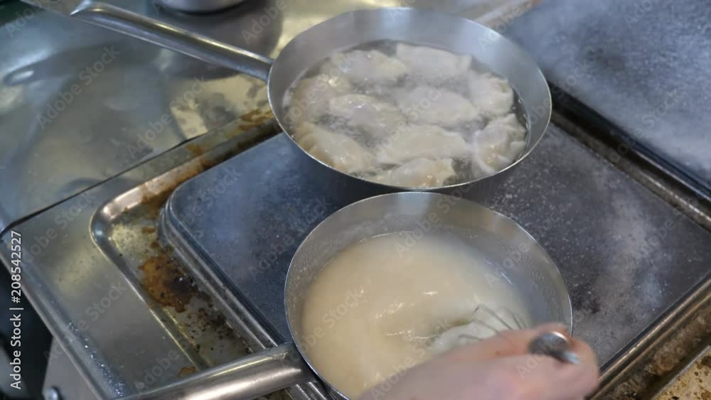 A professional chef prepares food in the kitchen of the restaurant in stainless steel dishes. Preparation of dumplings and cream sauce. Cooking process. A professional chef prepares food in the kitchen of the restaurant in stainless steel dishes. Preparation of dumplings and cream sauce. Cooking process.