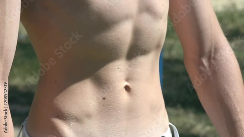 Young sexy guy shows his strong abdominal muscles during workout exercise in a Park