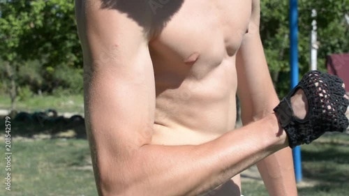 Young sexy guy shows his strong abdominal muscles during workout exercise in a Park