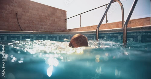 Young boy with goggles swimming in swimming pool in summer