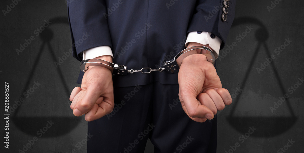 Arrested businessman in handcuffs with hands behind back and justice symbol wallpaper
