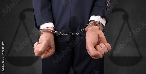 Arrested businessman in handcuffs with hands behind back and justice symbol wallpaper  