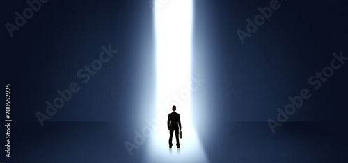 Businessman standing and seeing the light at the end of a big wall
