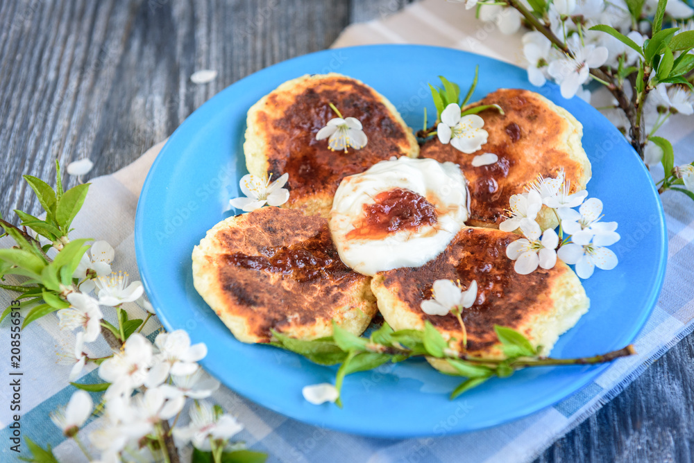 Homemade cottage cheese pancakes on blue plate with spring cherry plum branches on wooden background. Healthy breakfast or snack.