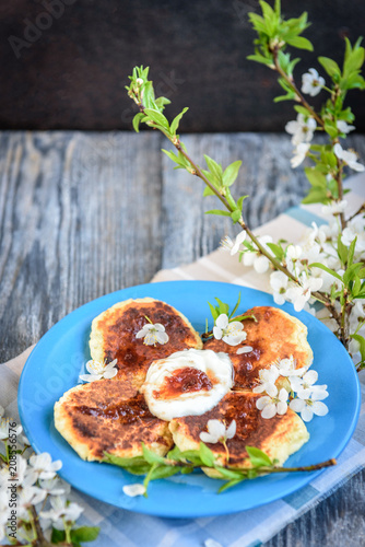 Homemade cottage cheese pancakes on blue plate with spring cherry plum branches on wooden background. Healthy breakfast or snack.