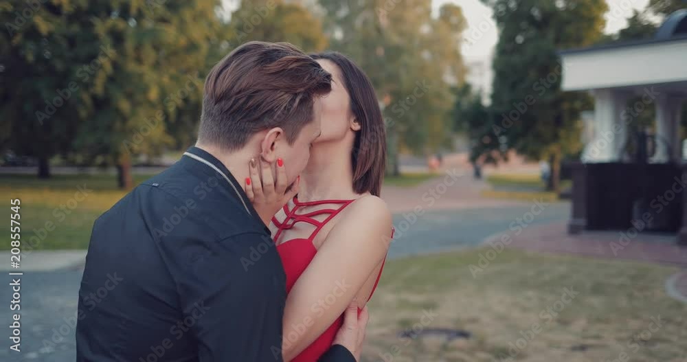 Girl kisses her beloved young man. Loving young couple in the park at sunset Girl kisses her beloved young man. Loving young couple in the park at sunset