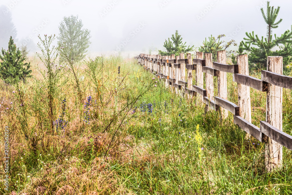 A misty morning in the countryside. A long wooden fence.