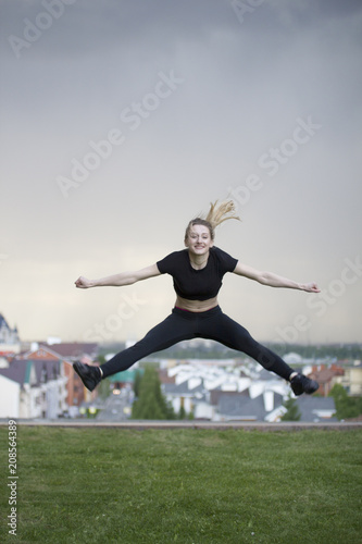 Young caucasian girl performs twine jumping over background cityscape