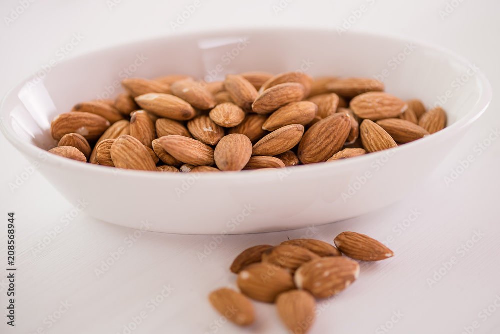 heap of almonds in white dish on white background heap of almonds in white dish on white background