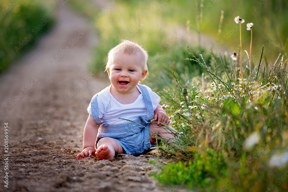 Sweet toddler boy, sitting on a rural path, exploring nature on sunset Sweet toddler boy, sitting on a rural path, exploring nature on sunset