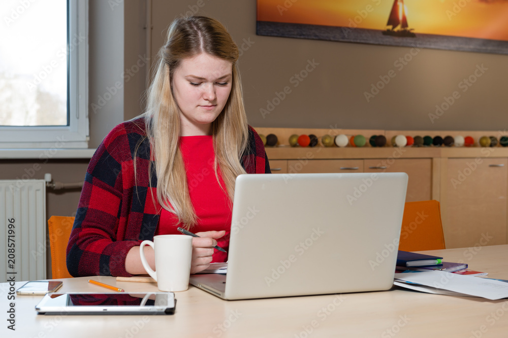 Smiling blonde woman sitting at a laptop drinking tea and working. Smiling blonde woman sitting at a laptop drinking tea and working.