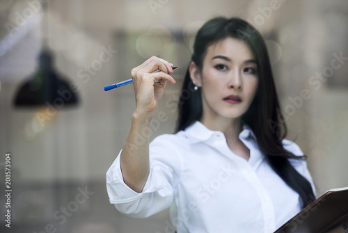 businesswoman writing or drawing something on blank glass board with pen marker