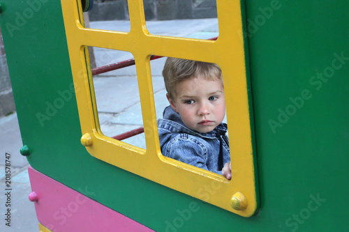 Children's phobias at the beginning of socialization. The kid looks sadly out the window. A sad child sits alone in a children's house on the playground.