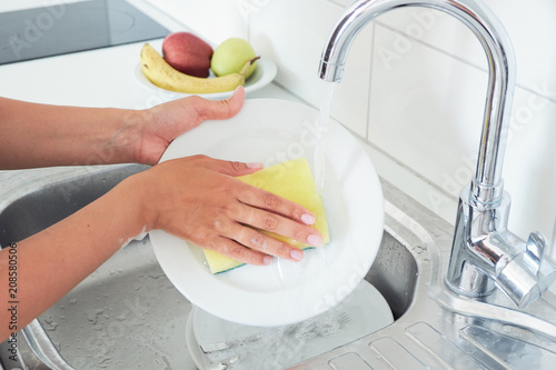 Cropped image of attractive young woman is washing dishes while doing cleaning at home