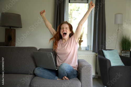 Konstfotografi Hübsche rothaarige Frau sitzt mit einem laptop auf ihrem Schoß auf einer Couch u