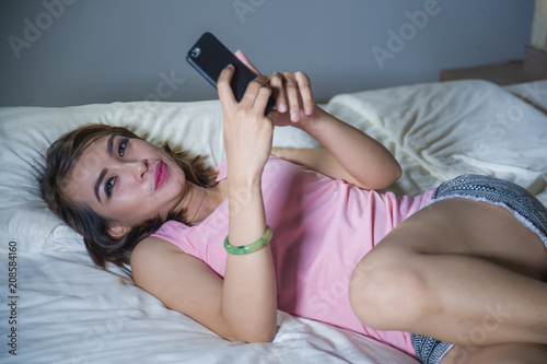 young beautiful and happy woman girl on bed smiling and flirting on internet social media app using mobile phone cheerful and relaxed on her bedroom