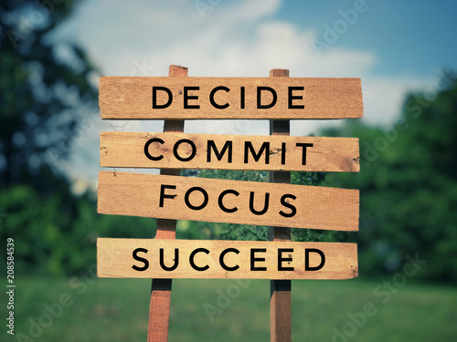 Motivational and inspirational quote - ‘Decide, commit, focus, succeed’ written on plank signage. With vintage styled background.