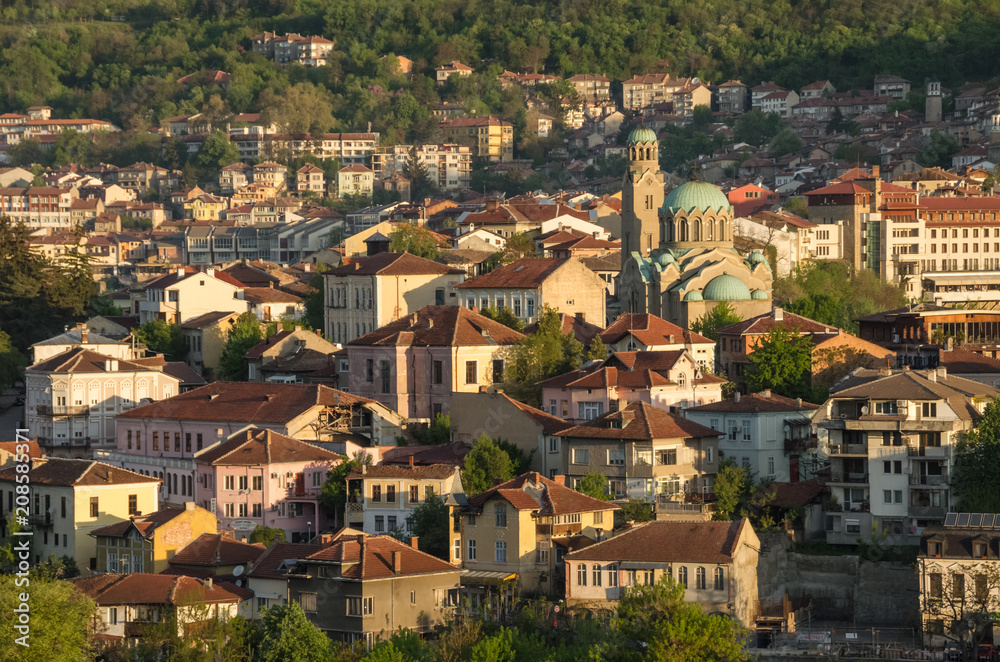 Scenic view at old town Veliko Tarnovo, Bulgaria. Traditional bulgarian architecture, tiled roofs are illuminated by the rising sun. Lovely spring morning. Main city cathedral on the background.