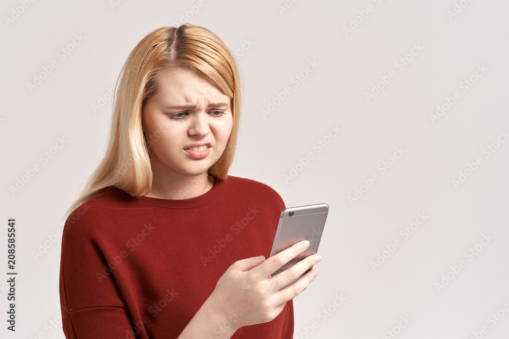 Worried upset nervous female model bites thumb, holds modern smart phone, feels frustrated as has failure of payment. Disappointed woman reads message about postponing or canceling interview Worried upset nervous female model bites thumb, holds modern smart phone, feels frustrated as has failure of payment. Disappointed woman reads message about postponing or canceling interview