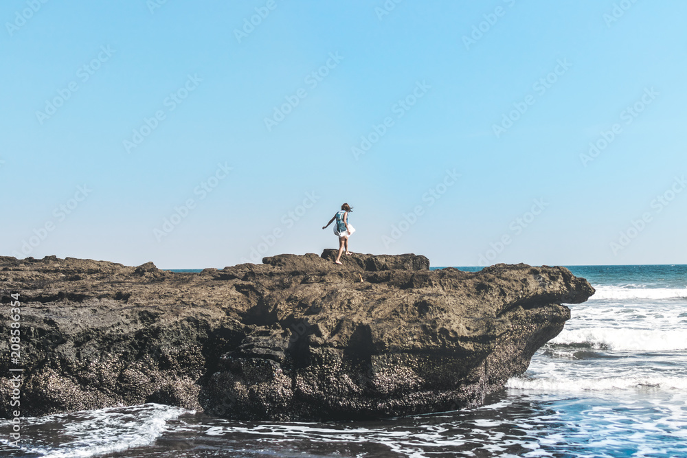 Young woman on the rock on a black sand beach, Bali island. Young woman on the rock on a black sand beach, Bali island.