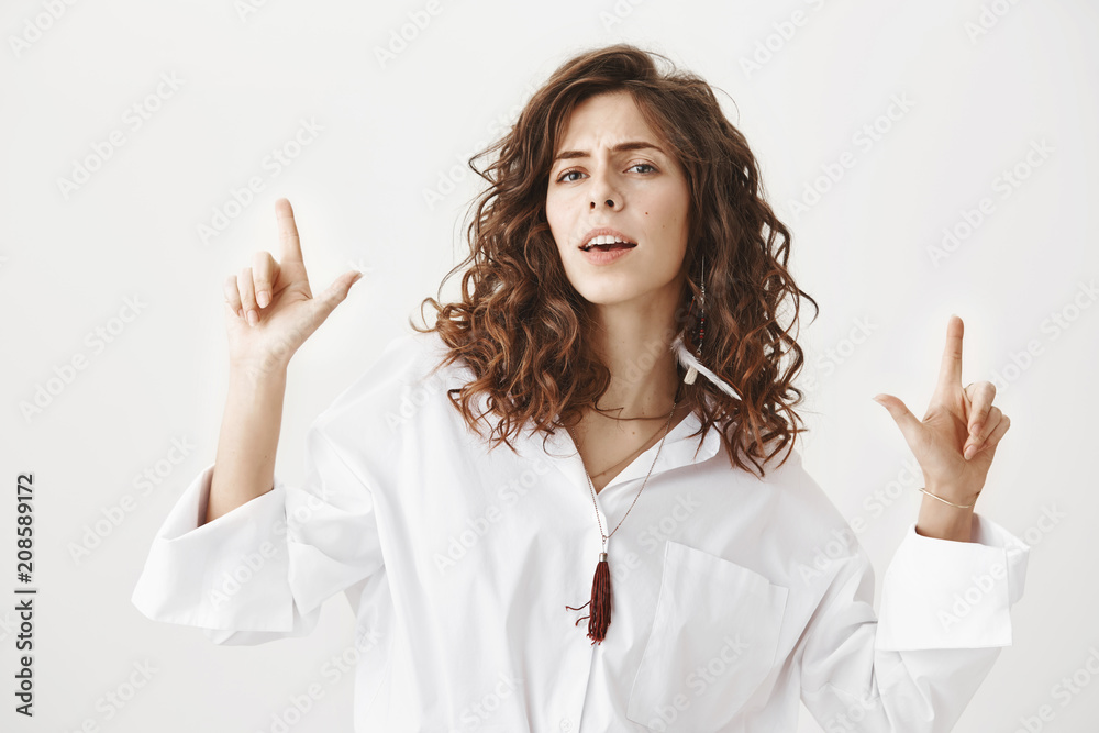 Portrait of confident cool caucasian woman pointing up or showing gun gestures with winner expression, frowning and acting like she is on top of world, standing over gray background. Portrait of confident cool caucasian woman pointing up or showing gun gestures with winner expression, frowning and acting like she is on top of world, standing over gray background.