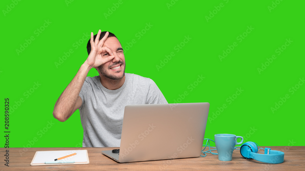 Happy young man sitting at his desk with a gesture of observe - Green background Happy young man sitting at his desk with a gesture of observe - Green background