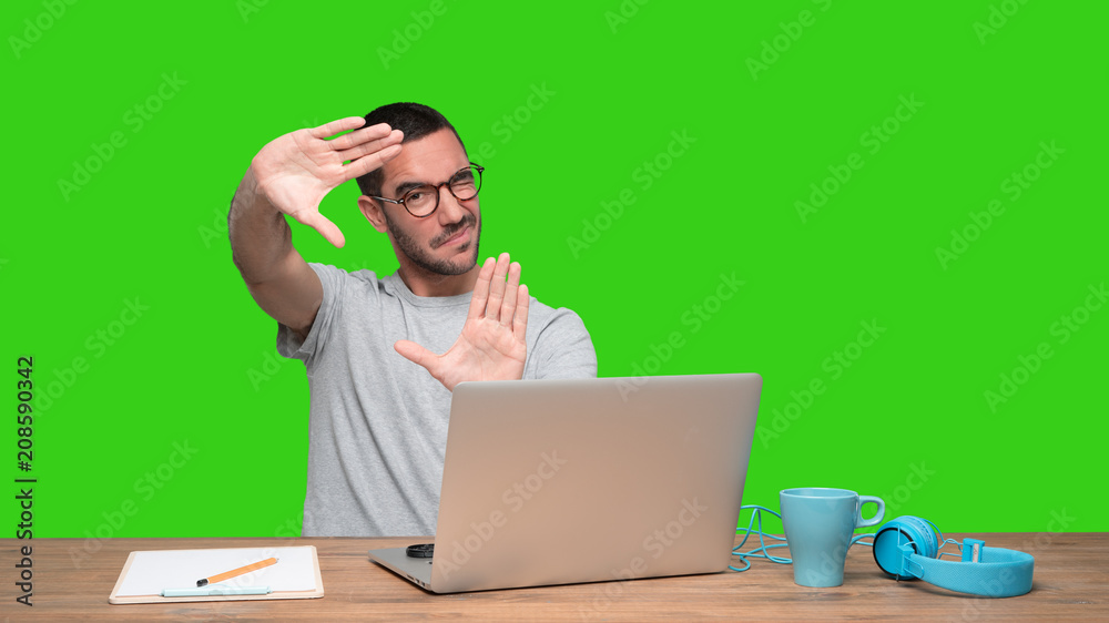Concentrated young man sitting at his desk doing a gesture of focusing with his hands - Green background