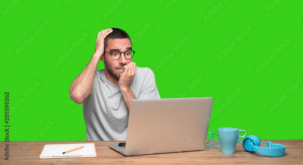 Nervous young man sitting at his desk - Green background