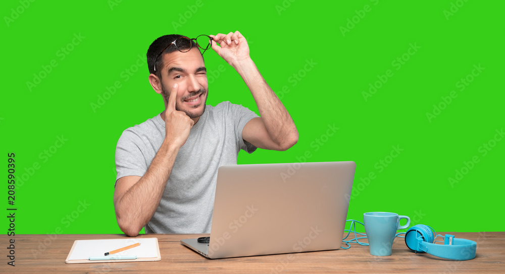 Concerned young man sitting at his desk and doing a gesture of observe - Green background Concerned young man sitting at his desk and doing a gesture of observe - Green background