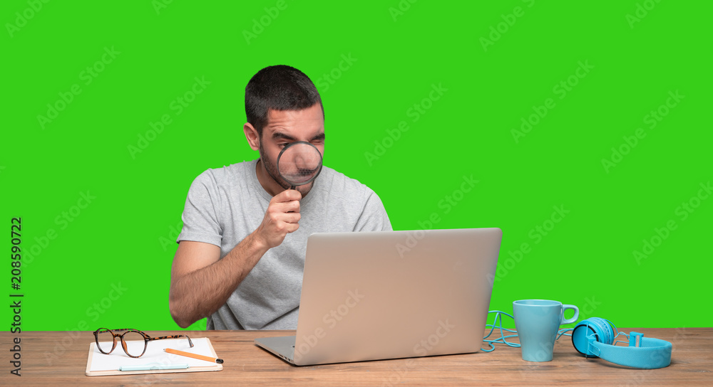 Concentrated young man using a magnifying glass on his laptop - Green background Concentrated young man using a magnifying glass on his laptop - Green background