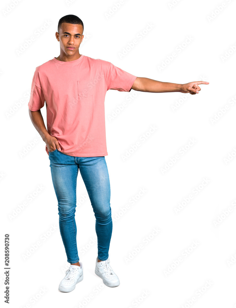 Standing young african american man pointing finger to the side and presenting a product on isolated white background Standing young african american man pointing finger to the side and presenting a product on isolated white background