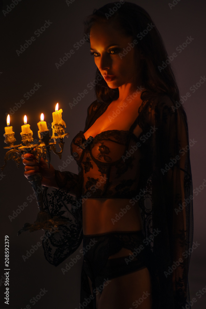 Brunette woman in black lace lingerie with candelabrum posing on dark background