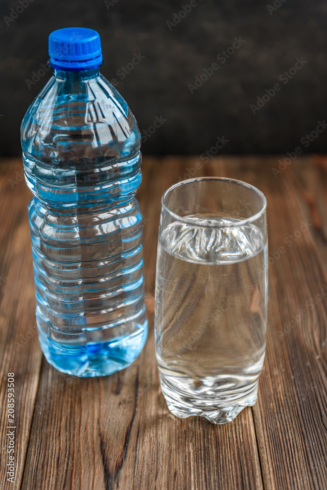Bottle and glass of water on wooden background with copy space.