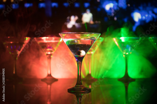 Several glasses of famous cocktail Martini, shot at a bar with dark toned foggy background and disco lights. Club drink concept © zef art