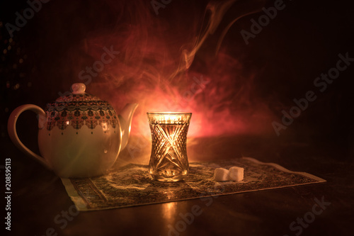 Eastern tea in traditional glasse and pot on black background with lights and smoke. Eastern tea concept. Armudu traditional Azerbaijan/Turkish cup