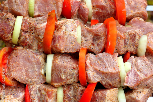Pieces of marinated raw pork meat strung on skewers with slices of chopped tomatoes and onion prepared for cooking on barbecue. Raw meat
