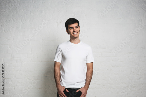 Smiling man in white blank t-shirt in studio. White wall