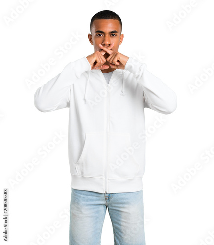 Dark-skinned young man with white sweatshirt showing a sign of closing mouth and silence gesture on isolated white background © luismolinero