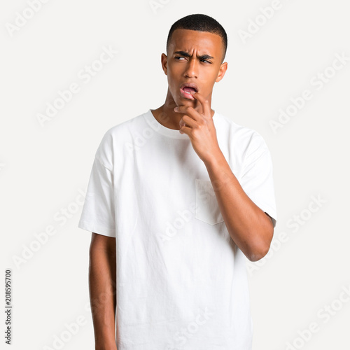 Young african american man having doubts and with confuse face expression while looking up. Questioning an idea on isolated background